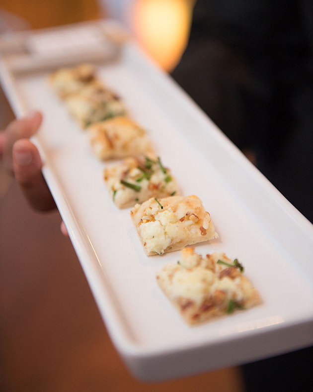 A white plate held in hand showing small savory pastry appetizers topped with herbs, warm ambient lighting, inviting mood